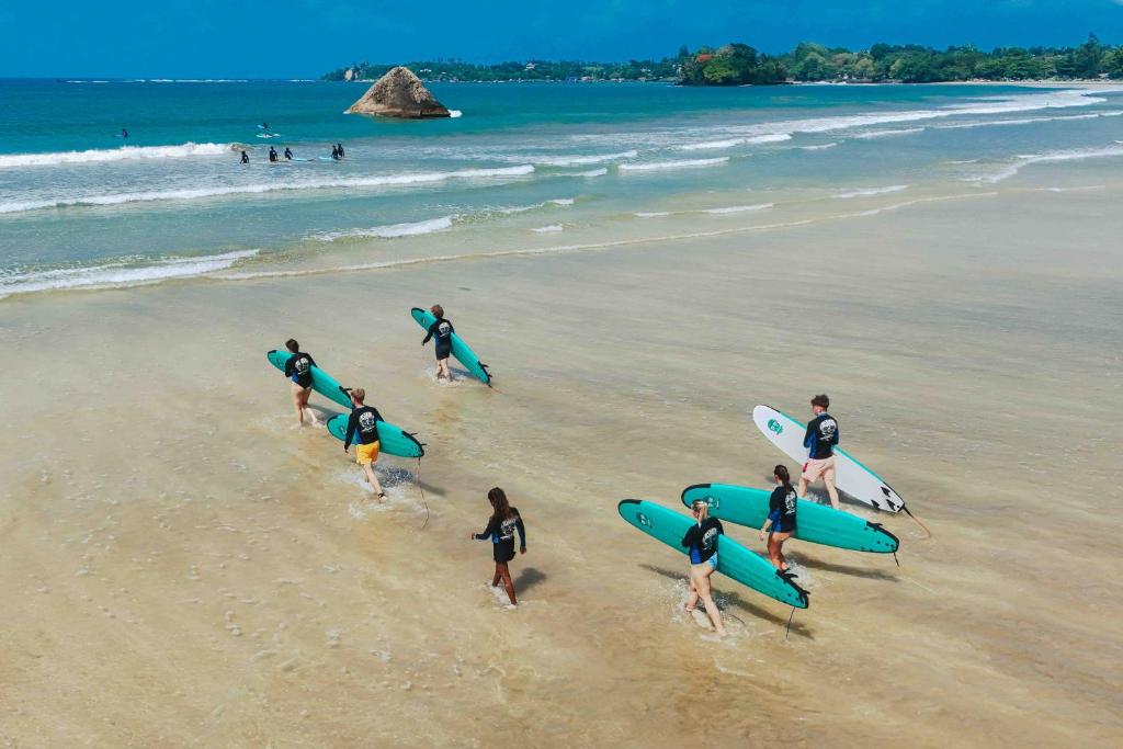 Surfers and beachgoers at Weligama beach with Taprobane Island in the background.