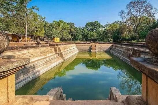 Ancient stone carved Kuttam Pokuna Twin Ponds surrounded by shaded trees in Anuradhapura.