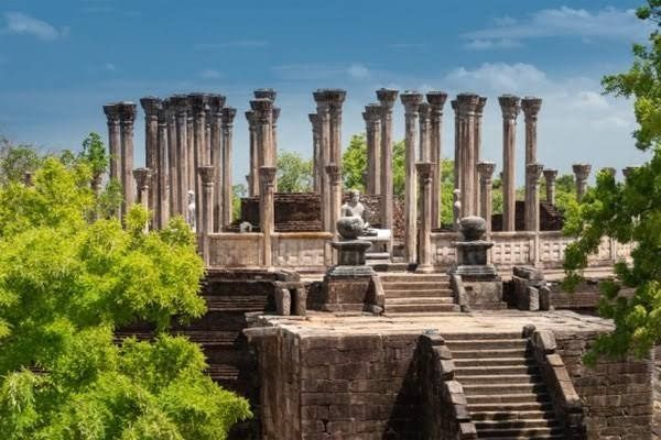 Ancient carved granite pillars and lush green pathways of the Polonnaruwa archaeological zone.