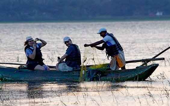 Tradizionale catamarano di legno che attraversa un lago ricoperto di fiori di loto durante un tour in un villaggio rurale dello Sri Lanka