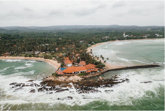 Aerial view of Dikwella coastal peninsula, resorts, and ocean waves breaking along the reef