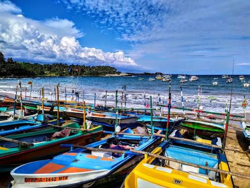 Vibrant multi-colored local fishing boats anchored along the coastal bay of Gandara under a dramatic cloudy blue sky
