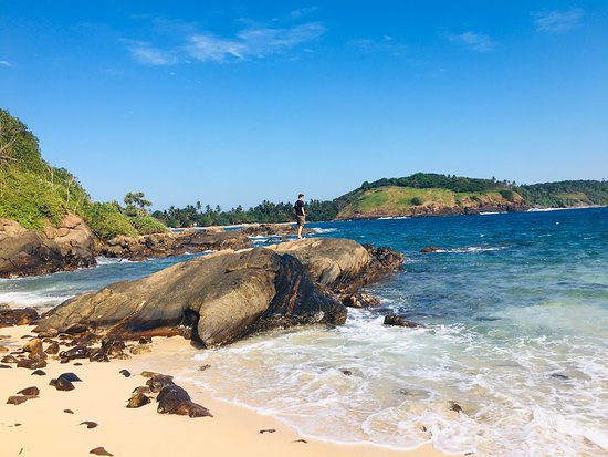 A traveler standing on coastal rock formations overlooking the turquoise ocean at Kudawella Beach