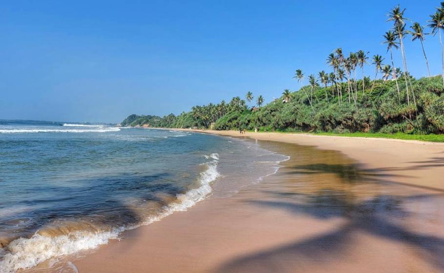 Pristine golden sands and gentle surf waves washing ashore at Lakshawaththa Beach under a clear blue sky