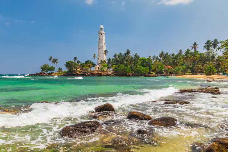 Historic white Matara lighthouse overlooking rocky shores and turquoise waves of the Indian Ocean