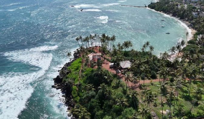 Aerial view of the palm-covered coastal peninsula and crashing white surf waves in Matara