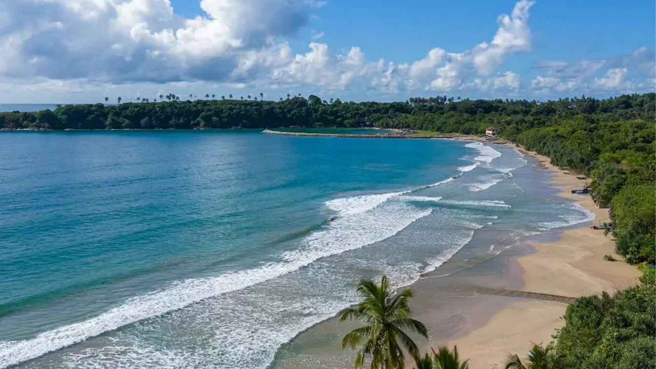 Aerial panoramic view of the expansive crescent curve, golden sand, and turquoise waters of Mawella Beach