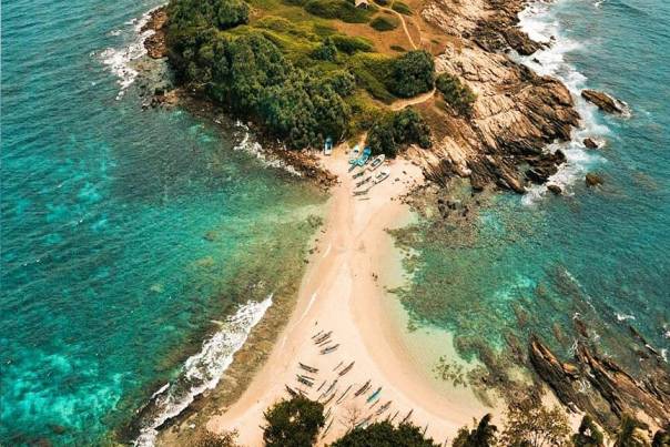 Aerial view of Nilwella Beach showing the stunning natural sand spit connecting to a green rocky islet surrounded by turquoise water