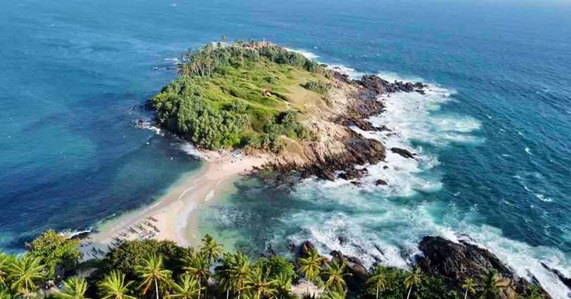 High-angle drone view of Nilwella rocky peninsula, pounding ocean waves, and the tranquil sand beach